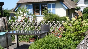 A house with a thatched roof, a wooden fence, and a table with a glass top.