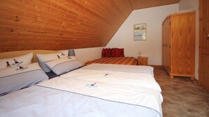 A bedroom with a sloped ceiling, two beds with matching bedding, a wooden wardrobe, and a small bedside table with a lamp.