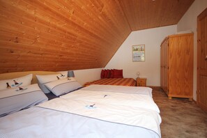 A bedroom with a sloped ceiling, two beds with matching bedding, a wooden wardrobe, and a small bedside table with a lamp. - On the beach, Germany (Wustrow)