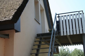 A building with a thatched roof, a white exterior, and a metal staircase leading to a balcony with a railing.