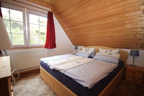 A bedroom with a bed, bedside tables, a window with curtains, and a radiator.
