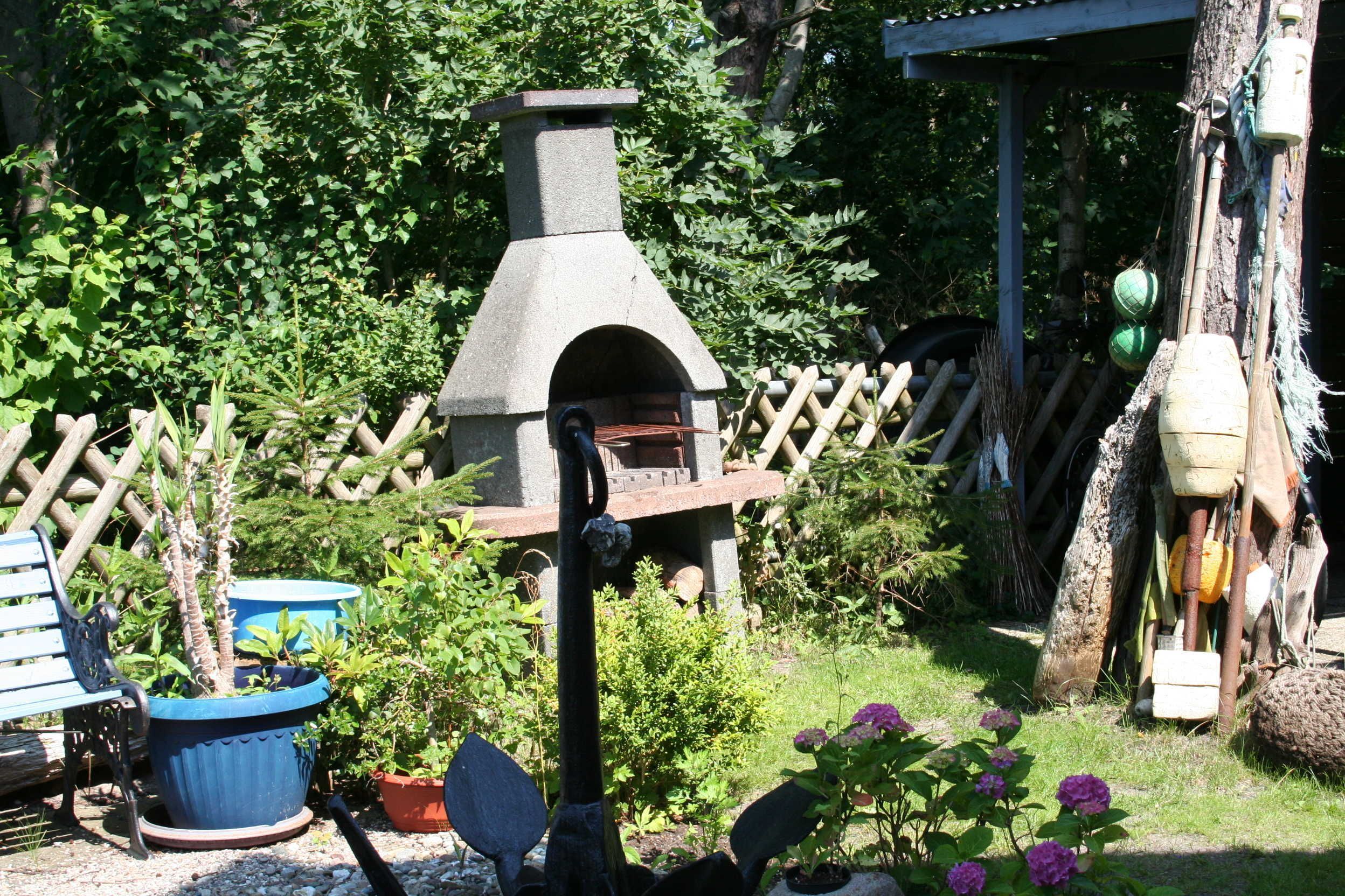A garden with a stone-built outdoor oven, potted plants, a wooden fence, and a rustic wooden structure.