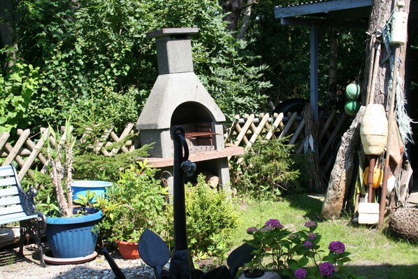 A garden with a stone-built outdoor oven, potted plants, a wooden fence, and a rustic wooden structure.