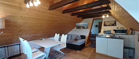 Ein gemütliches Zimmer im Mansardenstil mit Esstisch, Stühlen, einer Sitzecke und einer Küchenzeile.