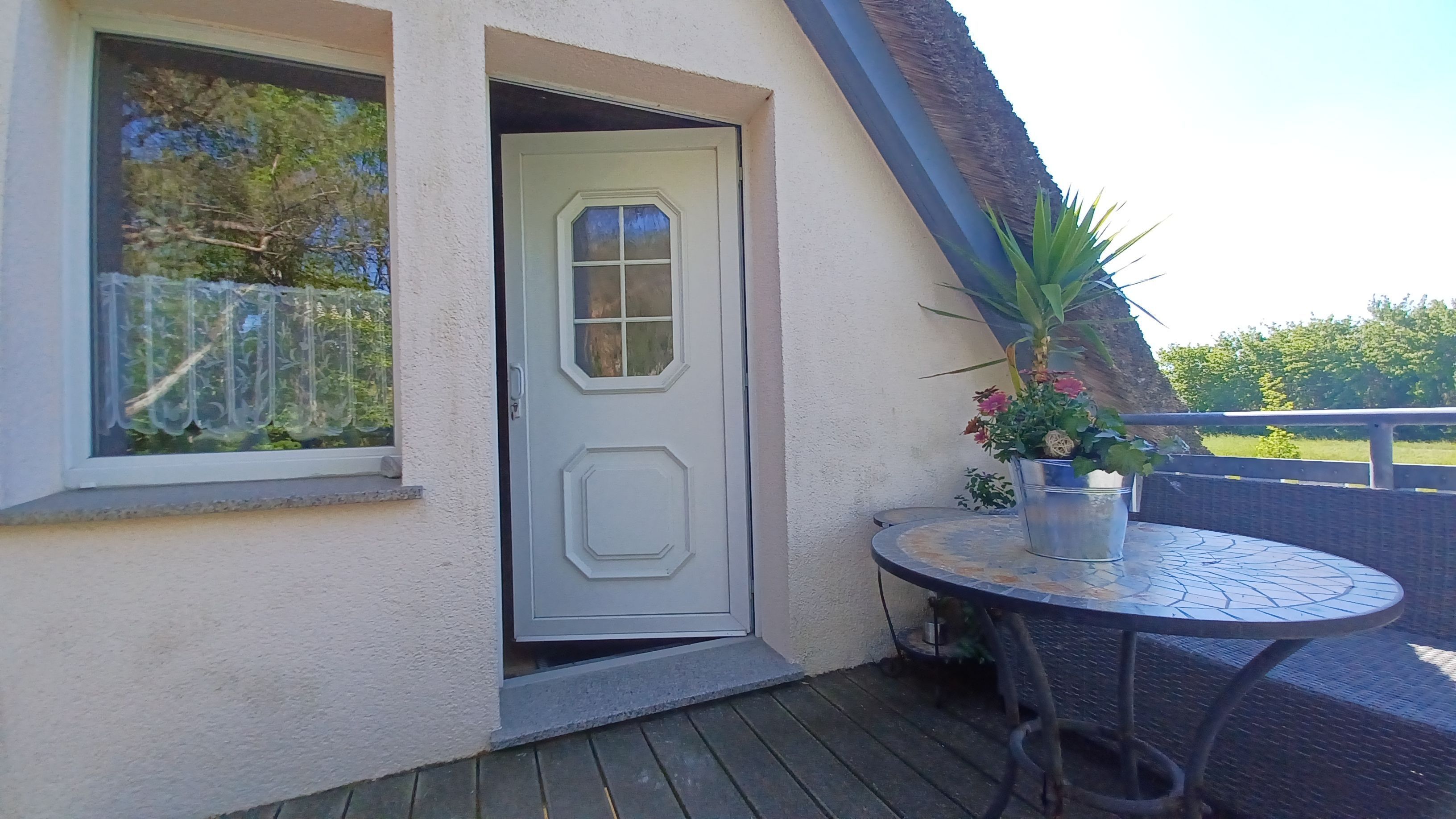 Eine Terrasse mit Tisch, Stühlen, einer Tür und einem Blumentopf.