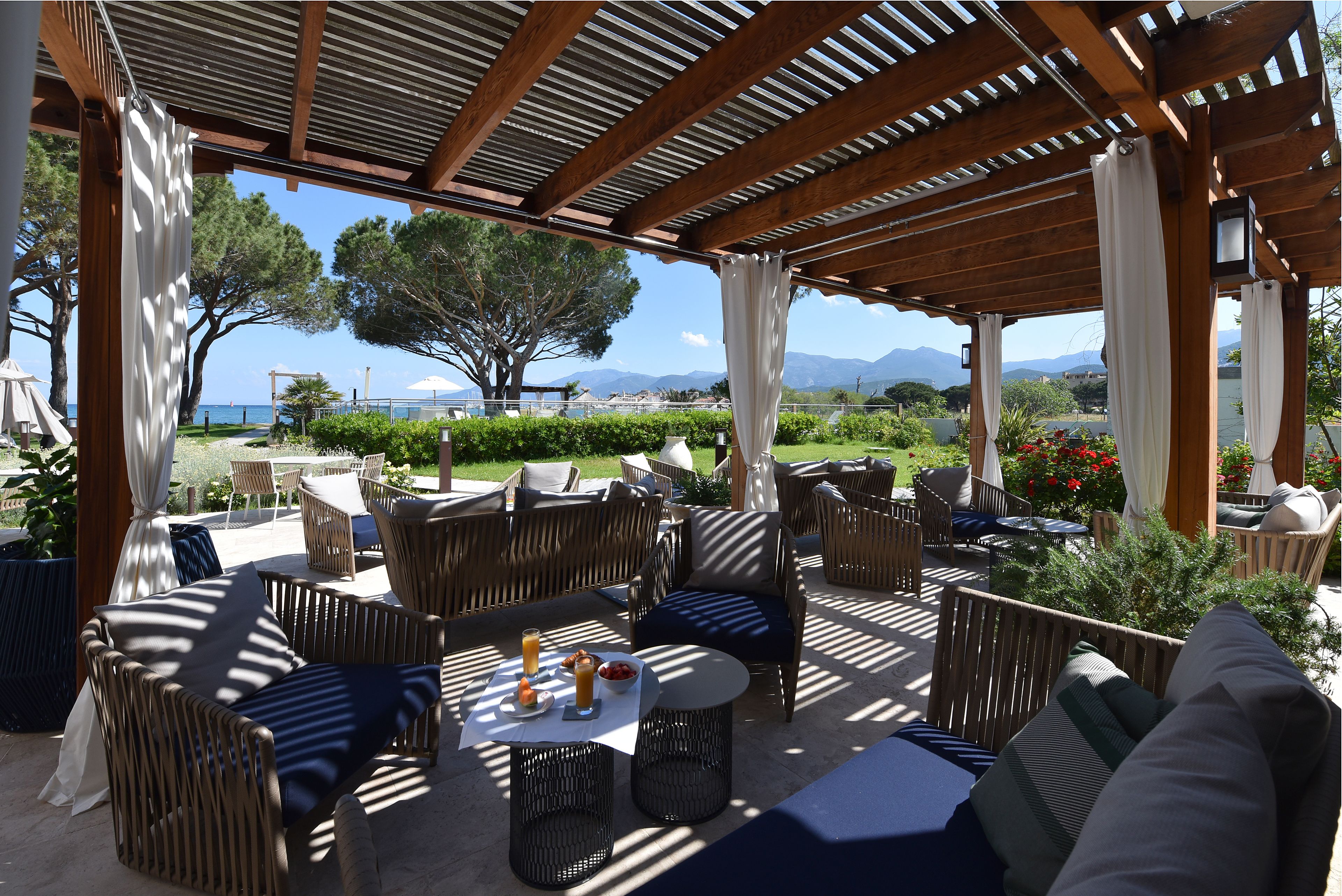 An outdoor patio with wicker furniture, a table with drinks, and a view of the sea and mountains.