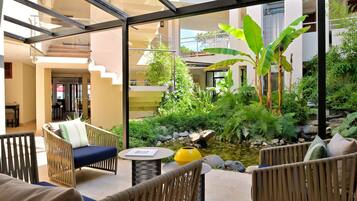 Un jardin intérieur moderne avec un petit étang, des meubles en osier et un escalier clos par des parois de verre.