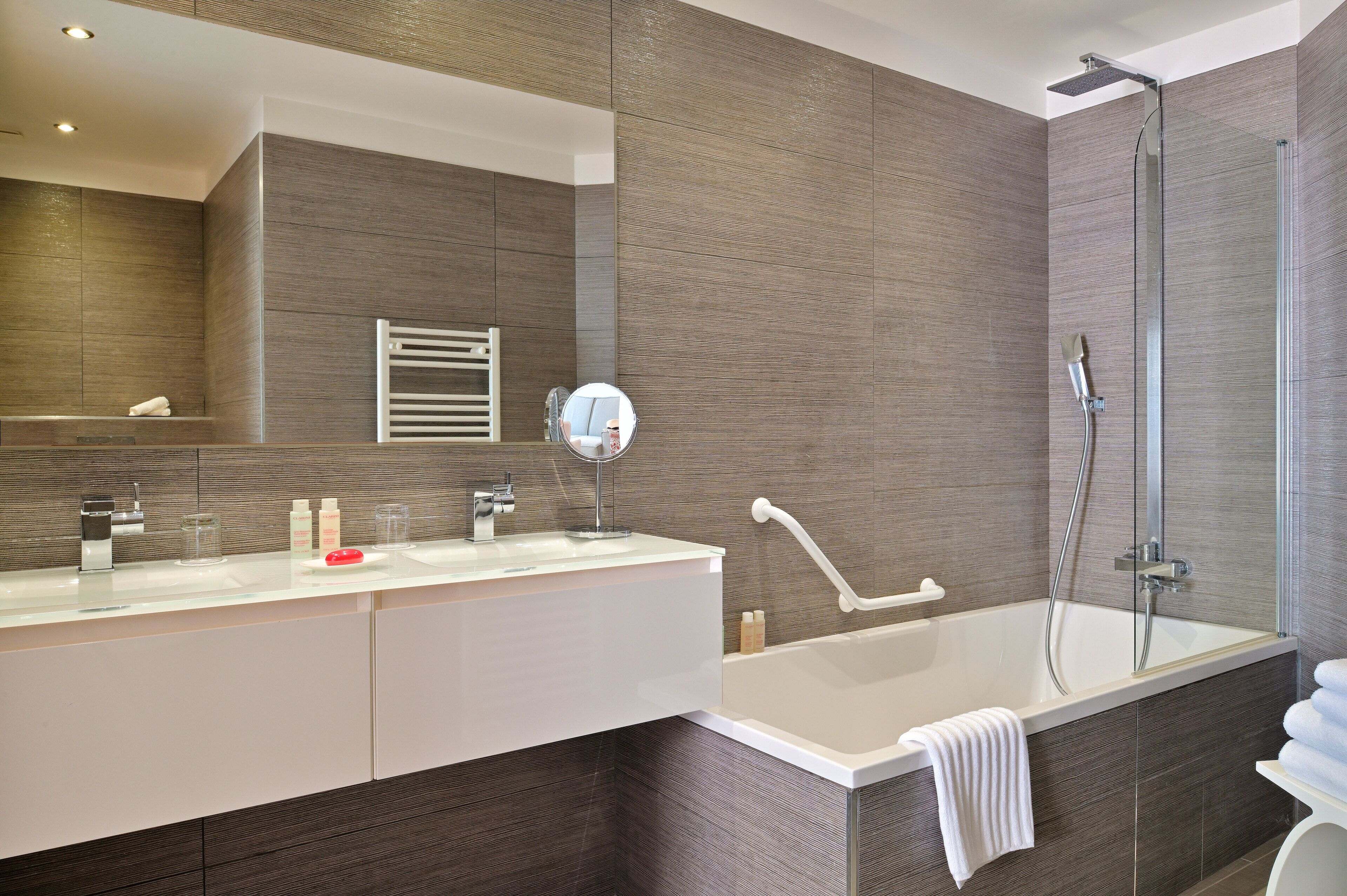 A modern bathroom with a large mirror, two sinks, a bathtub, and a shower.