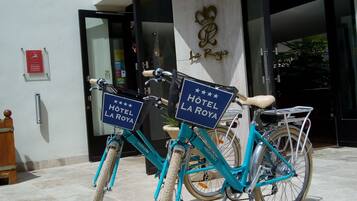 Two bicycles with "HOTEL LA ROYA" signs parked outside a building with a modern design, a glass entrance, and a sign indicating "GRANDES MAJORS" on the left.