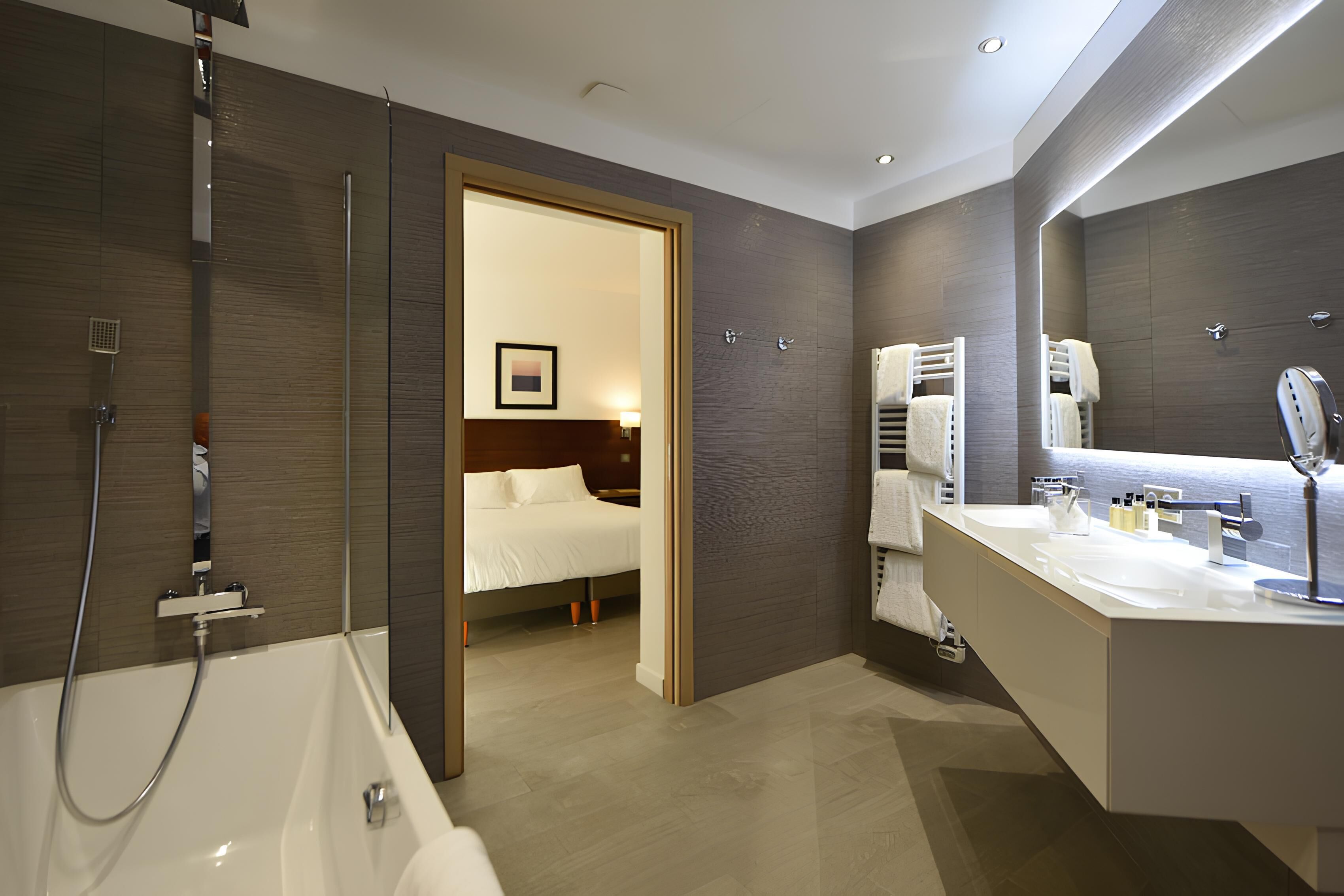 A modern bathroom with a bathtub, a large mirror, and a vanity with a sink.