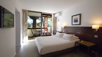 Habitación de hotel con una cama grande, una mesita de noche, una silla y vistas a un espacio exterior a través de una puerta de cristal.