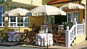 Un espace extérieur aménagé avec des tables et des chaises, protégé par des parasols, et un escalier menant à l’entrée d’un bâtiment.