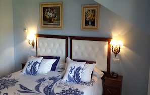 Ein Doppelbett mit geblattetem Kopfteil, zwei Wandlampen und zwei gerahmte Blumenbilder an der Wand.