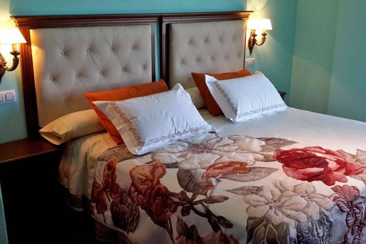 A bed with a floral bedspread, two white pillows, and an ornate headboard.