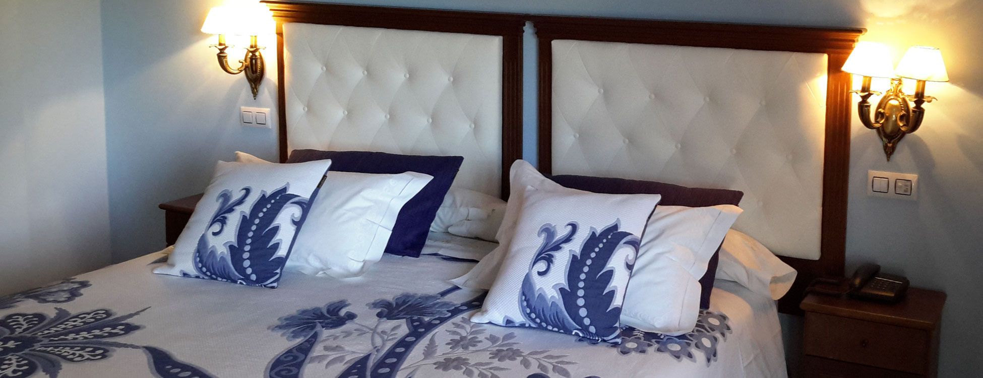 A double bed with a tufted headboard, two bedside lamps, and decorative pillows.