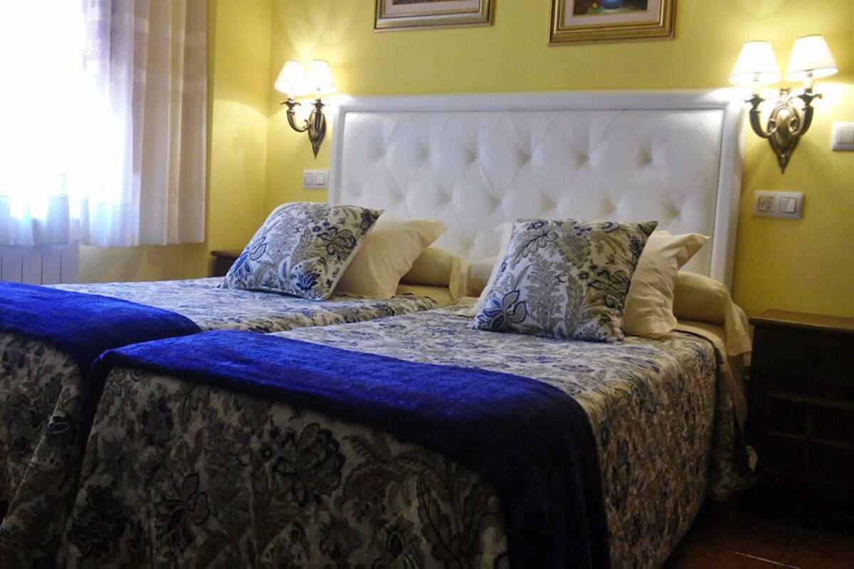 A double bed with a tufted headboard, two bedside lamps, and patterned bedspreads.