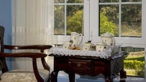 Une pièce avec une chaise en bois, une petite table recouverte d’une nappe en dentelle et une fenêtre donnant sur un paysage verdoyant.