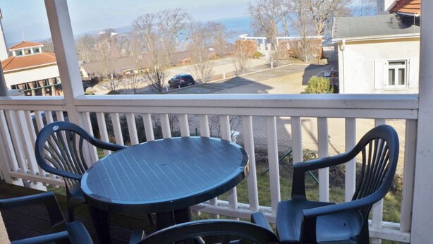 A covered outdoor area with a table and chairs, overlooking a residential street with houses and a parked car.