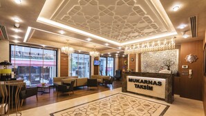 Rebedor d'hotel amb taulell de recepció amb el nom "MUKARNAS TAKSIM", mobles moderns, penjants i grans finestres que donen vista a l'exterior.