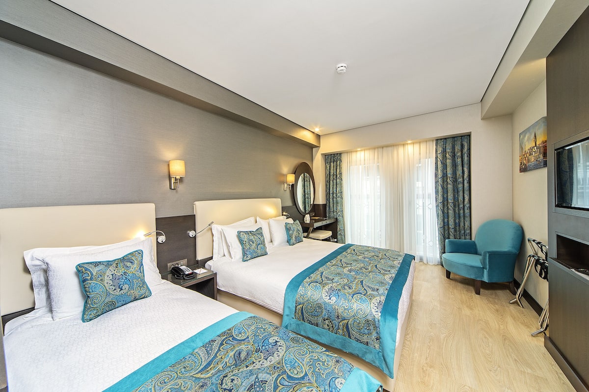 A hotel room with two beds, a TV, a chair, and a mirror.