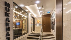 Interior d'un hotel modern amb una escala que condueix a la planta superior, una recepció i un senyal amb la inscripció 'MUKARNAS TAKSIM'.