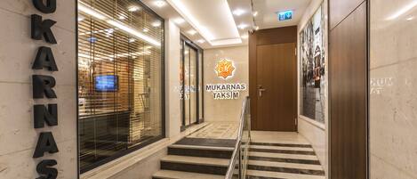 A modern hotel interior with a staircase leading to the upper floor, a reception desk, and a sign for 'MUKARNAS TAKSIM'.