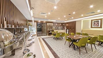 Un comedor moderno con mesas de buffet, piso estampado y disposición de asientos con sillas verdes.