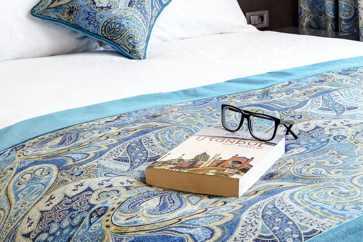 A neatly made bed with a patterned bedspread, a single pillow, and a book with glasses on it.