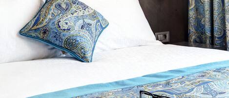 A neatly made bed with a patterned bedspread, a single pillow, and a book with glasses on it.