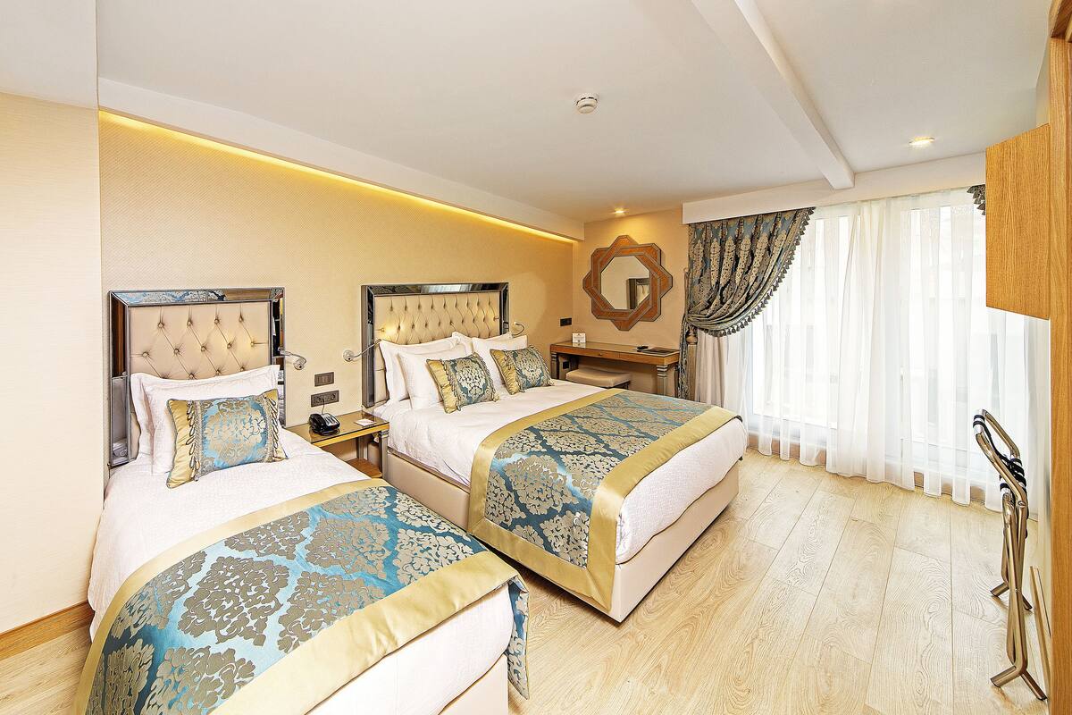 A hotel room with two beds, a nightstand, a mirror, and a window with curtains.