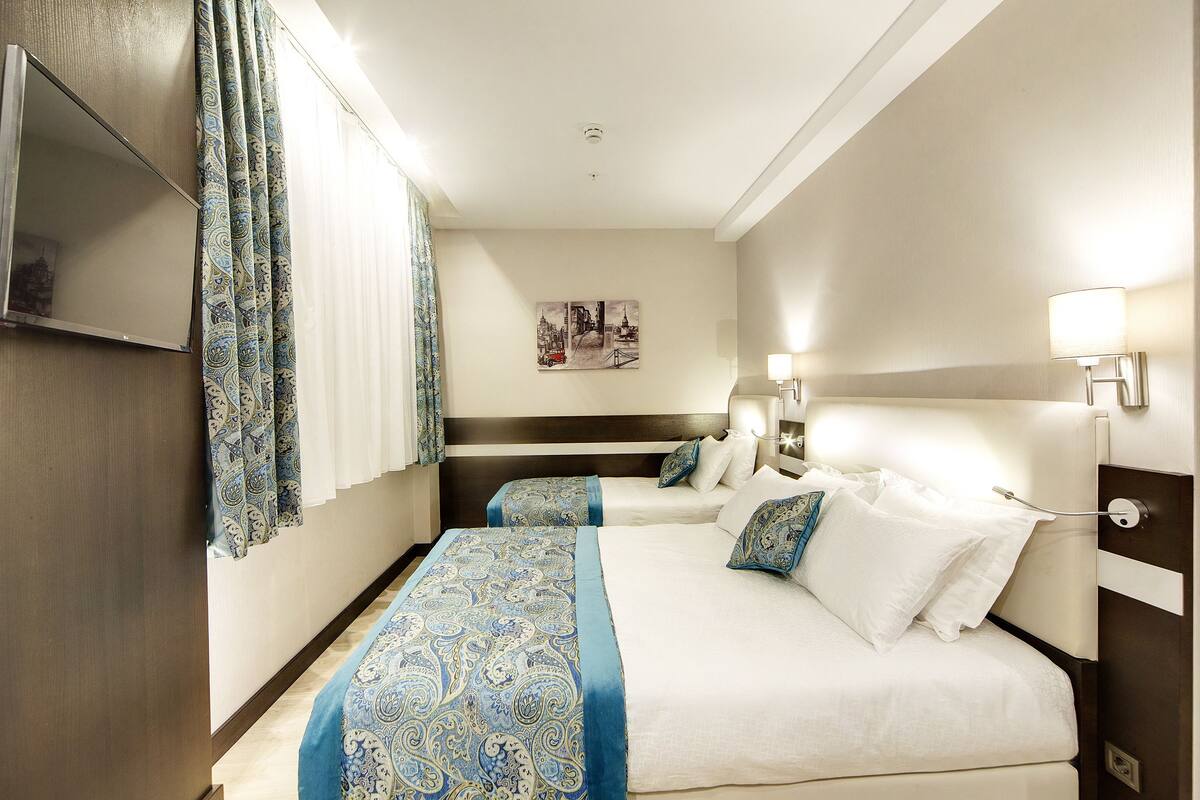A hotel room with two beds, a TV mounted on the wall, and a painting on the wall.