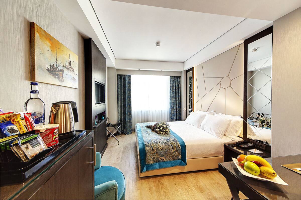 A modern hotel room with a bed, bedside table, and a desk with a computer.