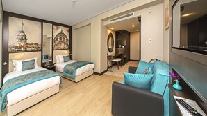Habitació d'hotel amb dos llits, un sofà, un escriptori i una televisió.