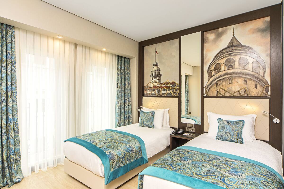 A hotel room with two beds, a large mirror, and artwork depicting a historical building.