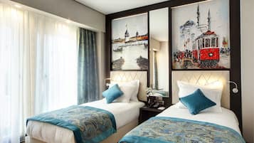 A hotel room with two beds, a large window with sheer curtains, and a wall with two framed paintings.