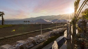 A beachside hotel with sun loungers, umbrellas, and a view of the ocean and mountains.