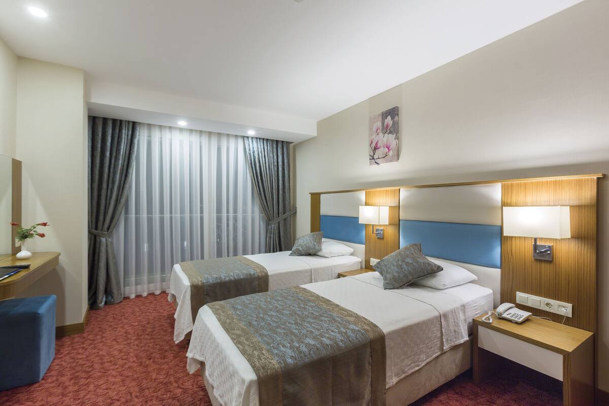 Habitación de hotel con dos camas, un escritorio, una silla, un teléfono y una ventana con cortinas.