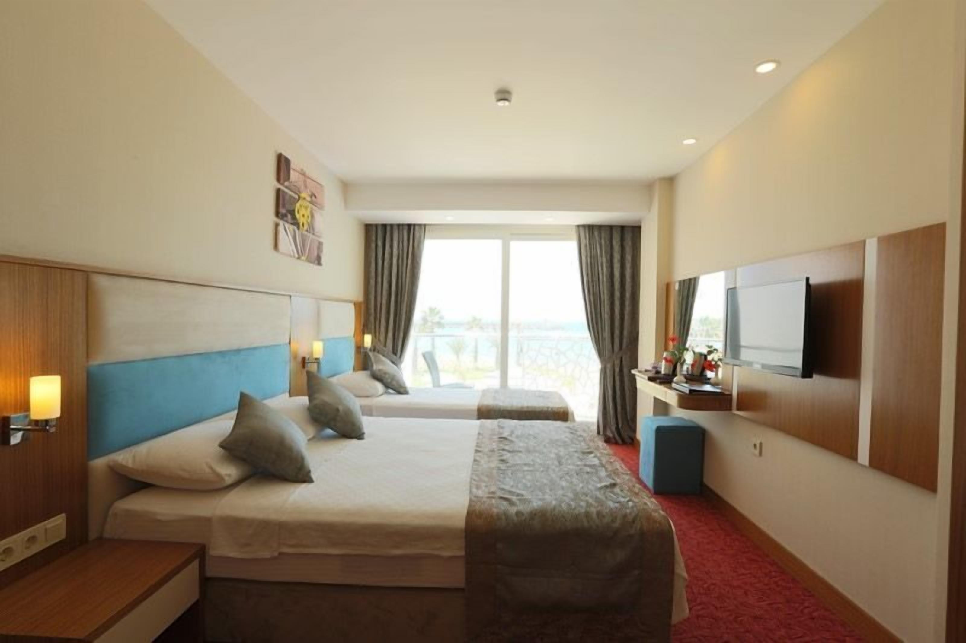 A hotel room with two beds, a TV, a desk, and a window with curtains.