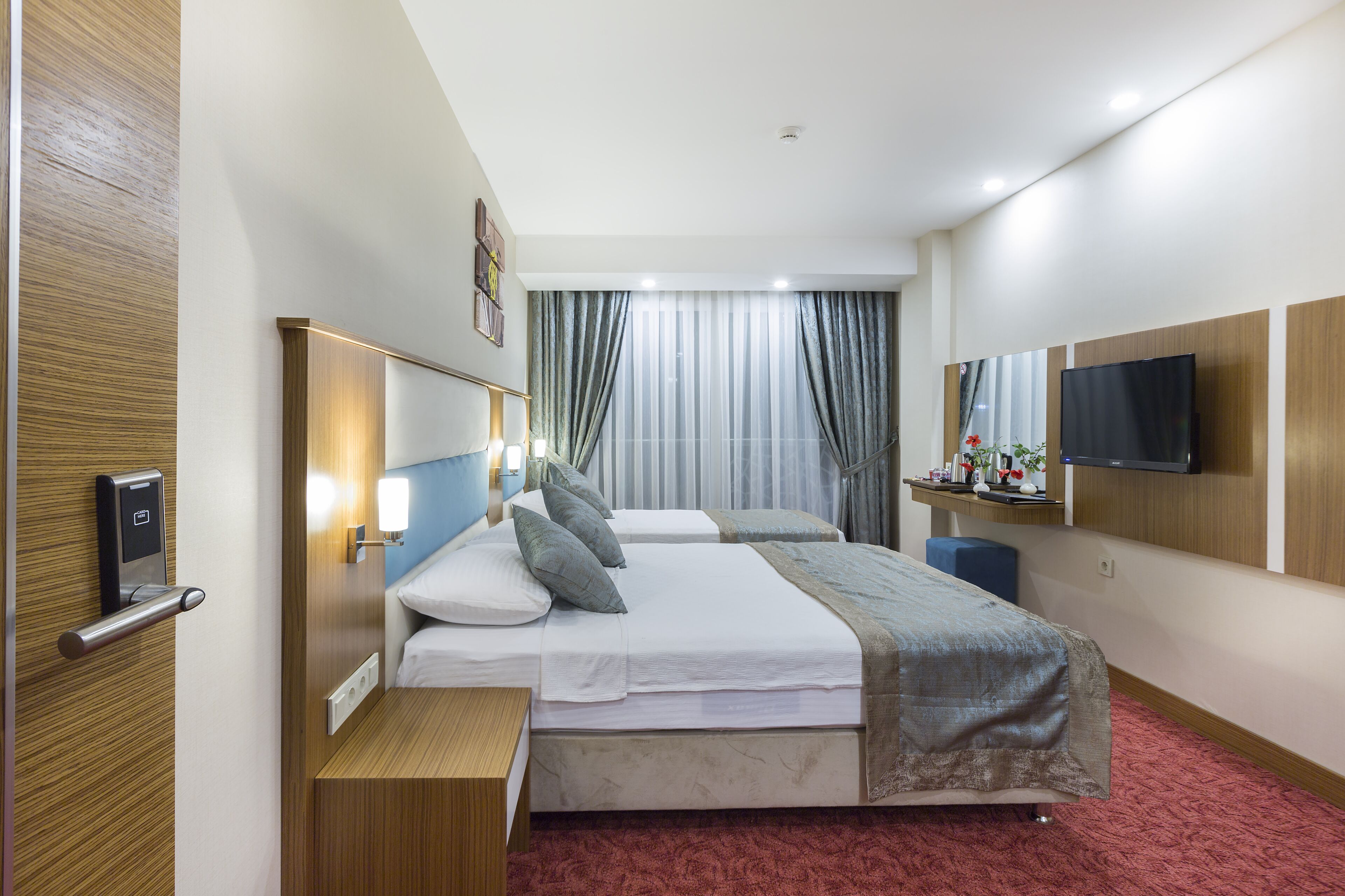 Ein Hotelzimmer mit zwei Betten, einem Fernseher, einem Schreibtisch und einem Spiegel.