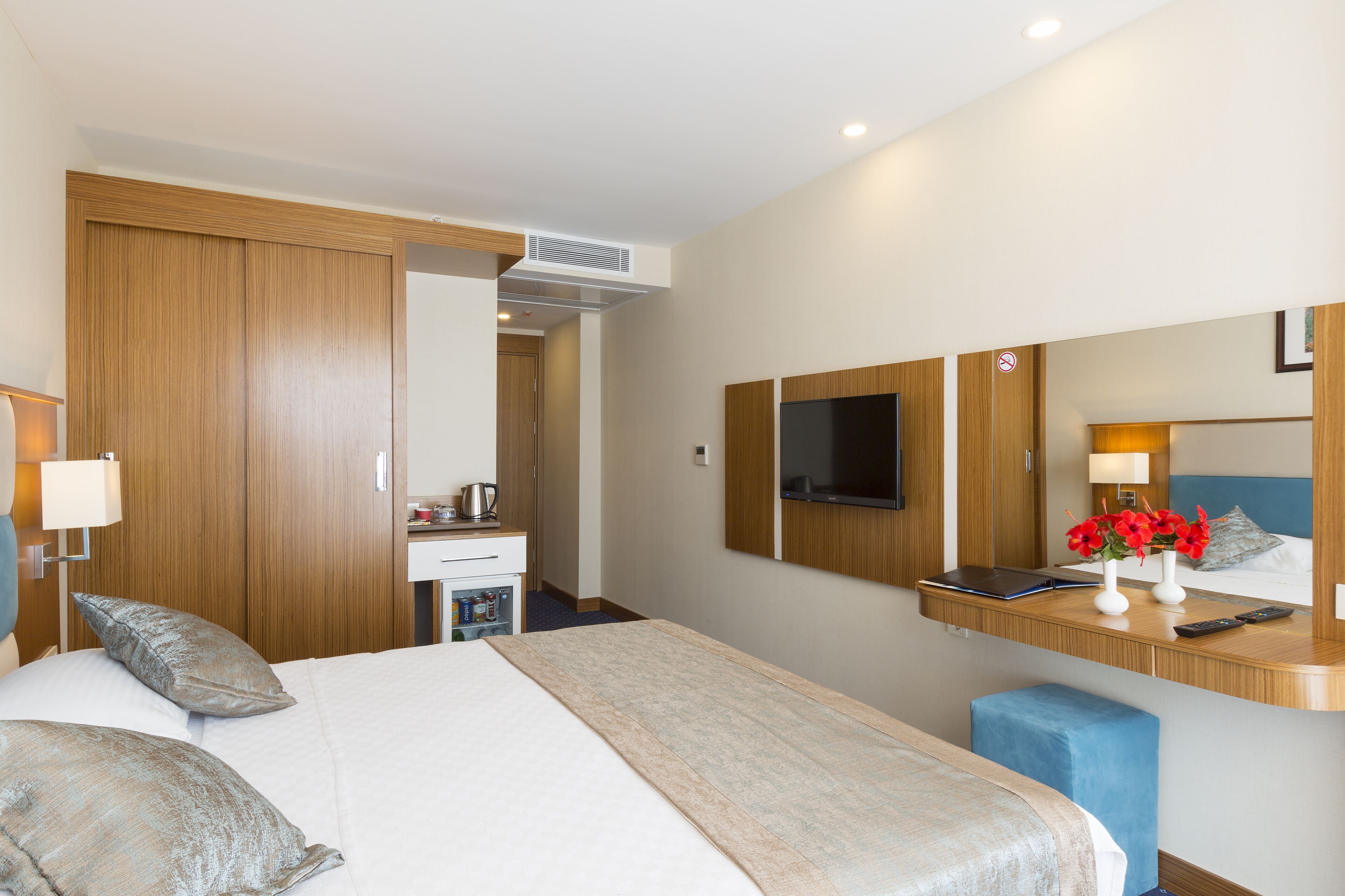 A hotel room with a bed, bedside table, TV, and a desk with a chair.