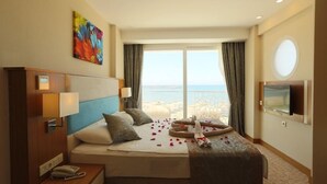 Habitación de hotel con cama, mesita de noche con teléfono, televisión y ventana con vista al mar.