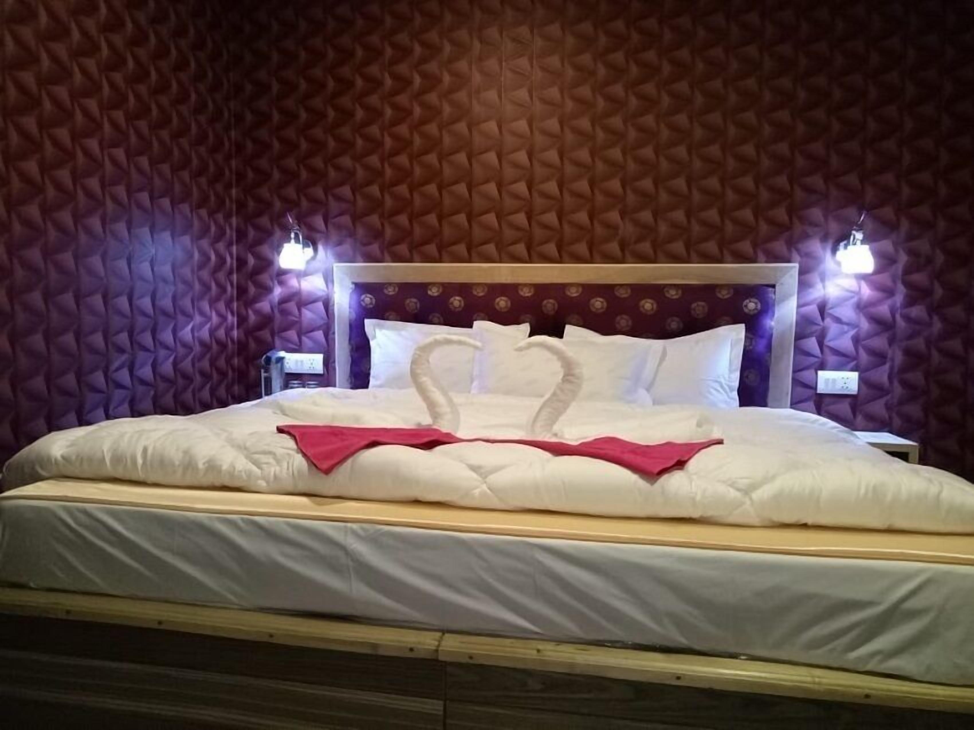 Habitación de hotel con cama, dos lámparas de noche y una decoración de almohadas con forma de cisne.