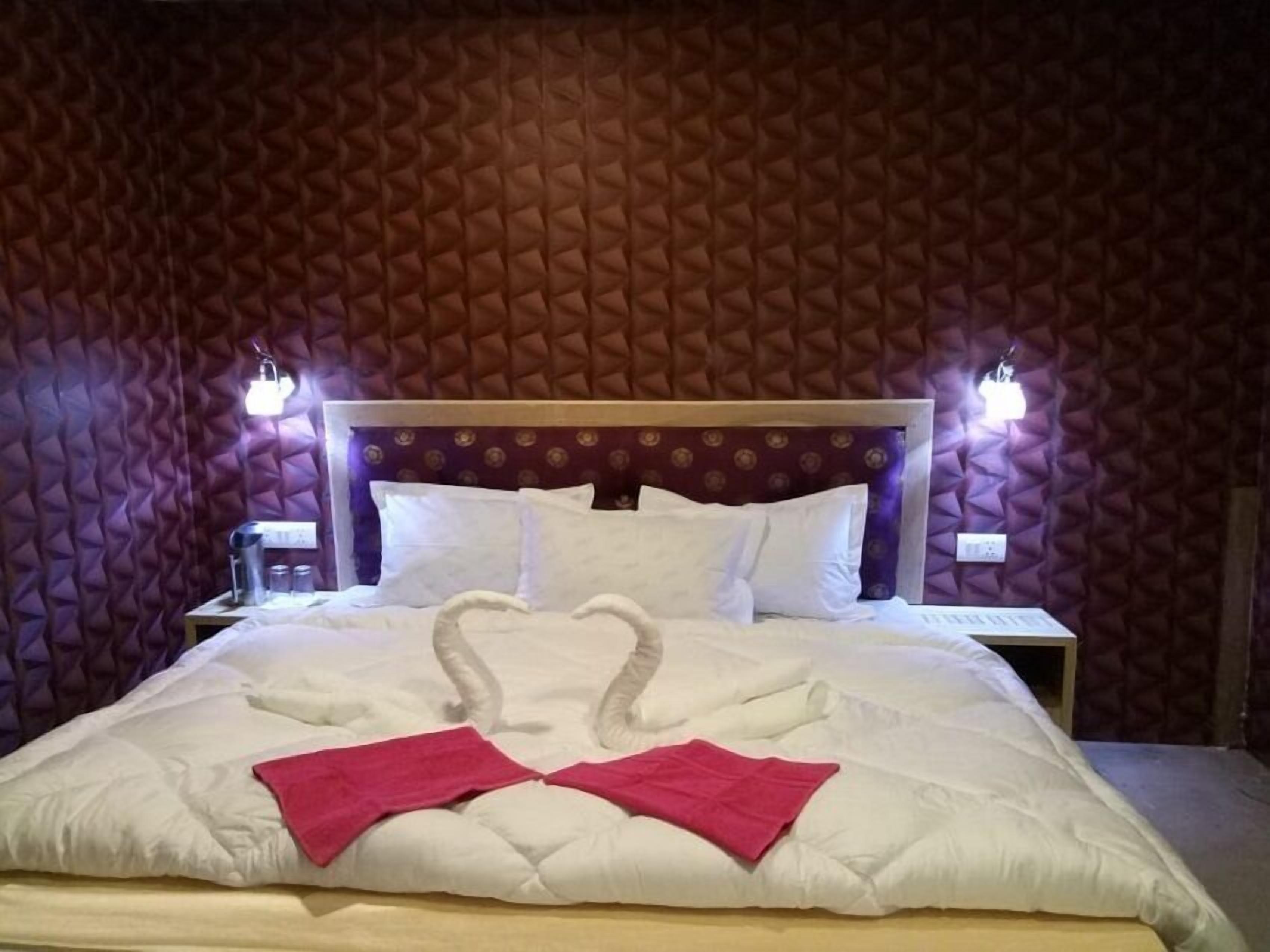 Una cama bien hecha con ropa de cama blanca y dos toallas rosas dispuestas en forma de corazón.