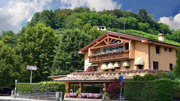 A two-story building with a balcony, surrounded by lush greenery and a mountainous backdrop. - Albergo Da Gildo (Follina)