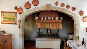 A rustic kitchen with an open fireplace, surrounded by copper pots and pans, and a dining area with a table set for two. - Albergo Da Gildo (Follina)