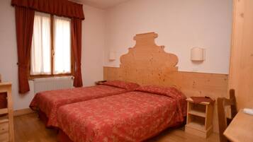 Une chambre avec deux lits, une tête de lit en bois, un radiateur, une petite table et une chaise.