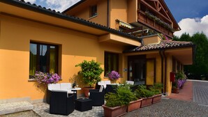 A two-story building with a yellow facade, outdoor seating area with black wicker furniture, and potted plants. - Albergo Da Gildo (Follina)