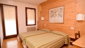 A room with two beds, wooden walls, a framed painting, and a window with curtains. - Albergo Da Gildo (Follina)