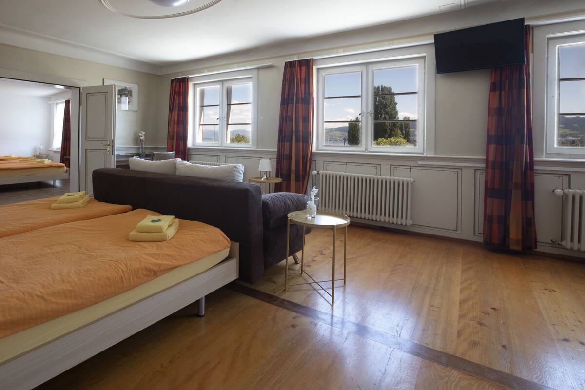 A hotel room with two beds, a sofa, a small table, a TV, and a window with curtains.