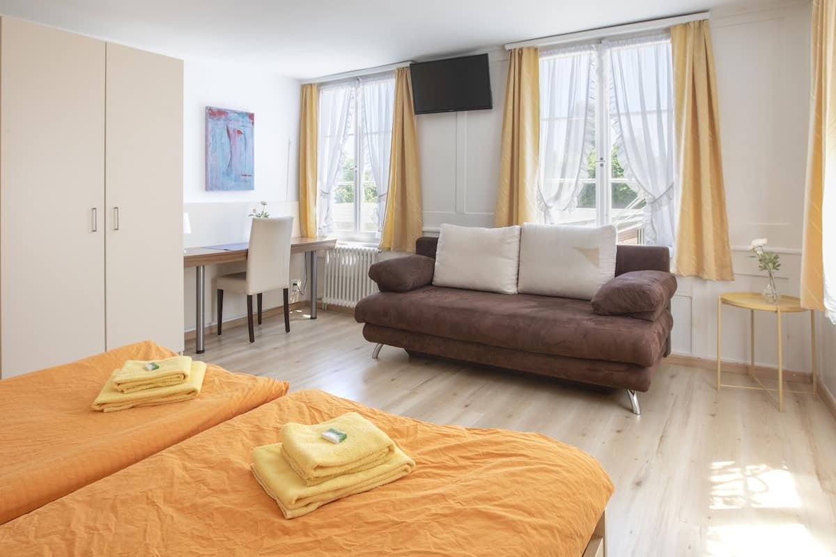 A hotel room with two beds, a sofa, a desk, and a TV.